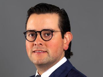 Man wearing glasses and a suit with a neutral background.