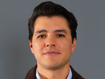Portrait of a young man with dark hair against a gray background.