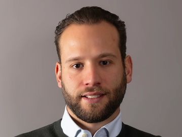 Portrait of a man with short hair and a beard against a gray background.