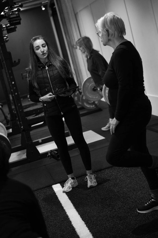 A fitness trainer instructs two women in a gym during a workout session.