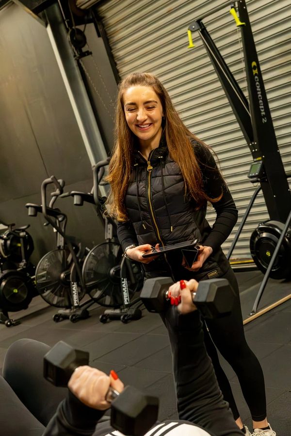 Personal trainer guiding a client lifting dumbbells in a gym.