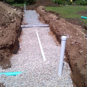 Trench with gravel and pipes being installed for drainage or plumbing.