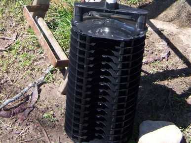 Black cylindrical garden tool with a wooden handle on soil.