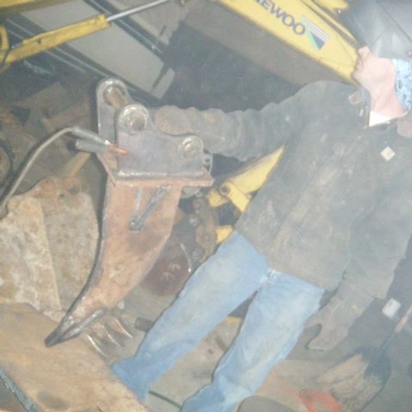 Welder working on excavator attachment in workshop.