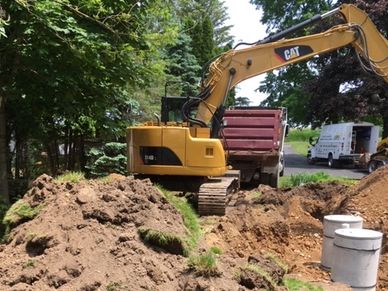 Excavator digging soil at a construction site with concrete pipes nearby.