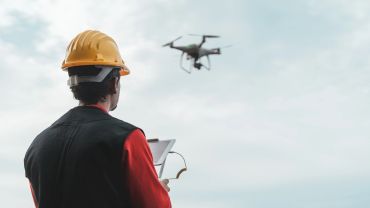 Persona con casco controla un dron en el aire.