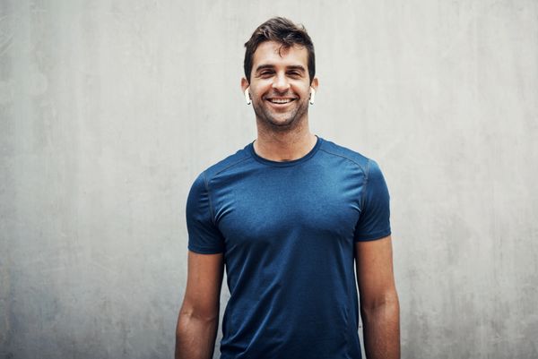 A young man standing against a grey wall while exercising outdoor