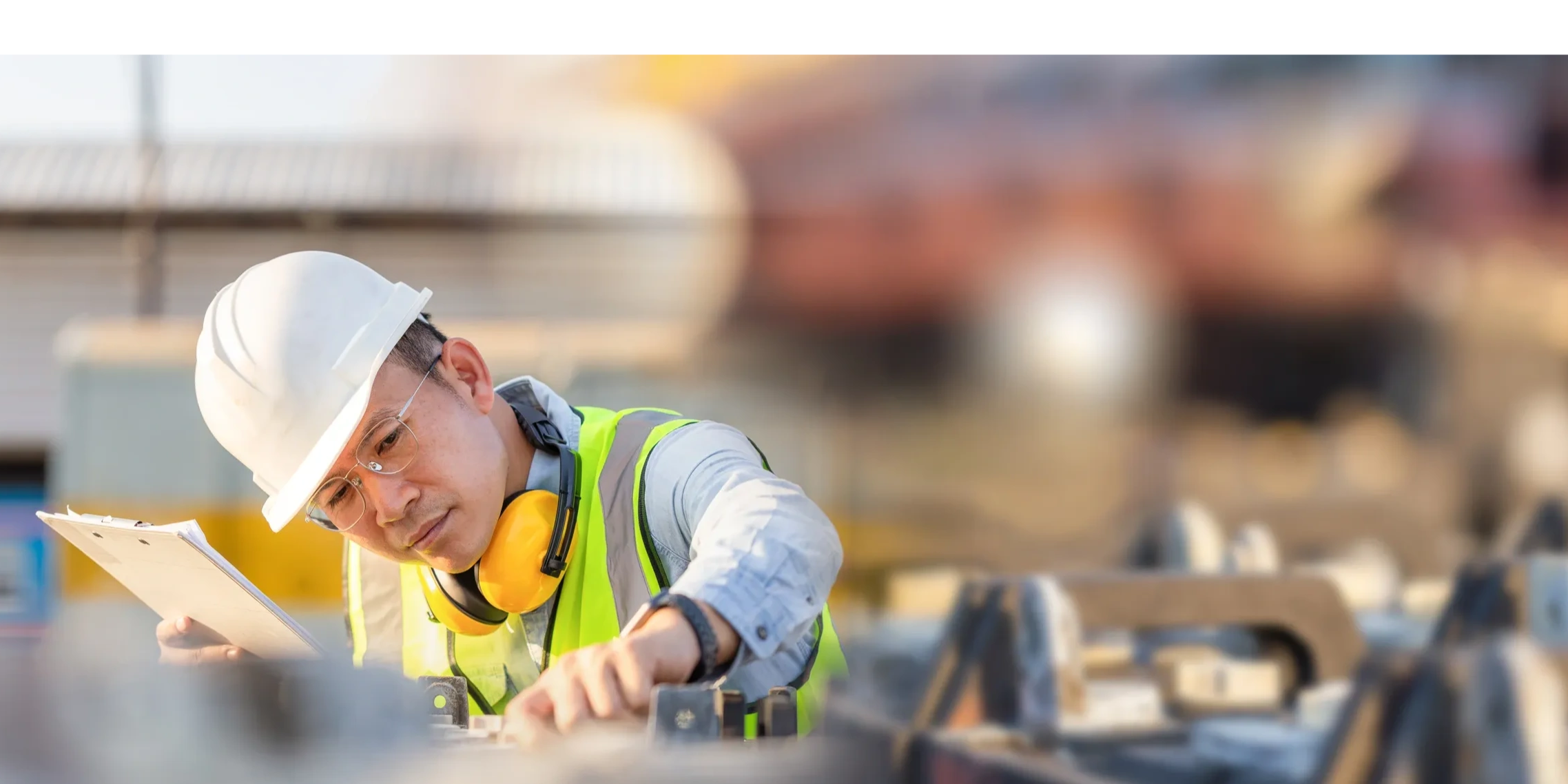 Engineer inspecting equipment on-site with a clipboard and safety gear.
