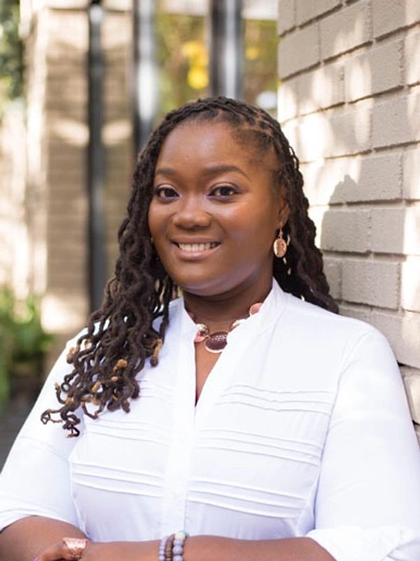 picture of a millennial black woman with a natural hair style, dressed in a white shirt and jewelry. 