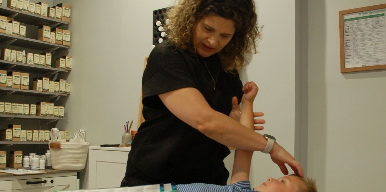Holistic practitioner Nicole performing muscle testing on a young child during a wellness consultati