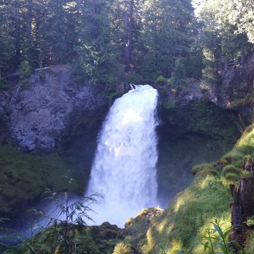 A powerful waterfall surrounded by lush green forest and rocky cliffs.