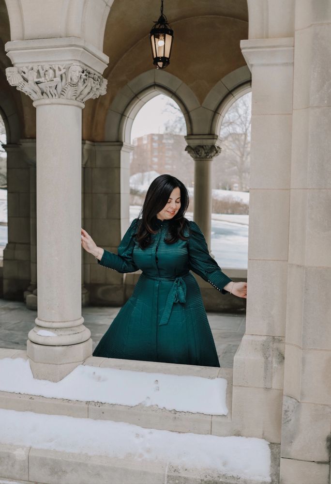 Woman in a teal dress poses gracefully among stone arches on a snowy day.