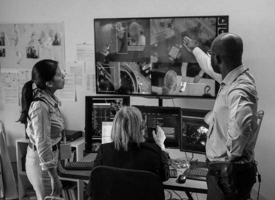Three professionals analyzing security footage on multiple monitors in a control room.