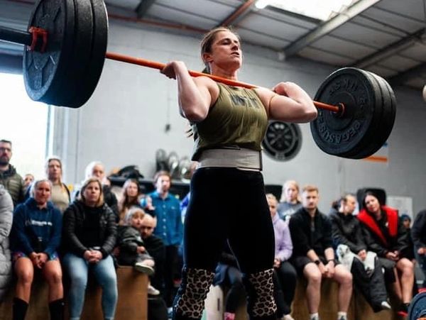 Woman lifting heavy barbell in a gym with an attentive audience.
