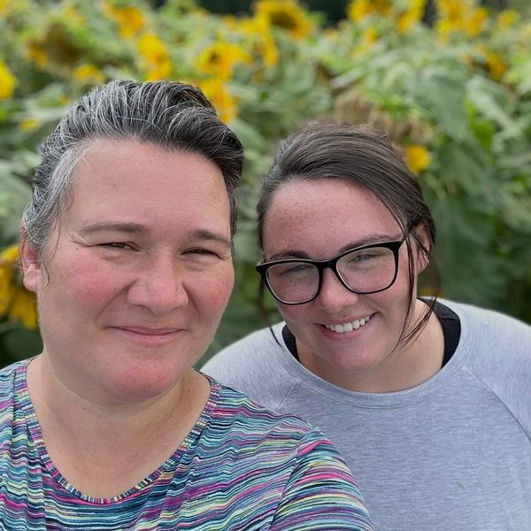 Two women smiling in front of sunflowers.
