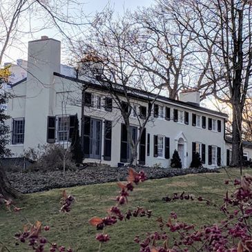 Elegant colonial-style estate home with white exterior and black shutters surrounded by mature trees