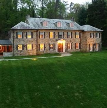 Expansive stone colonial estate with warm interior lighting, large front lawn
