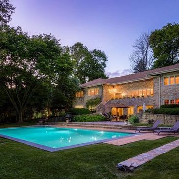 Luxury stone estate in Baltimore County with illuminated windows and a large backyard swimming pool 
