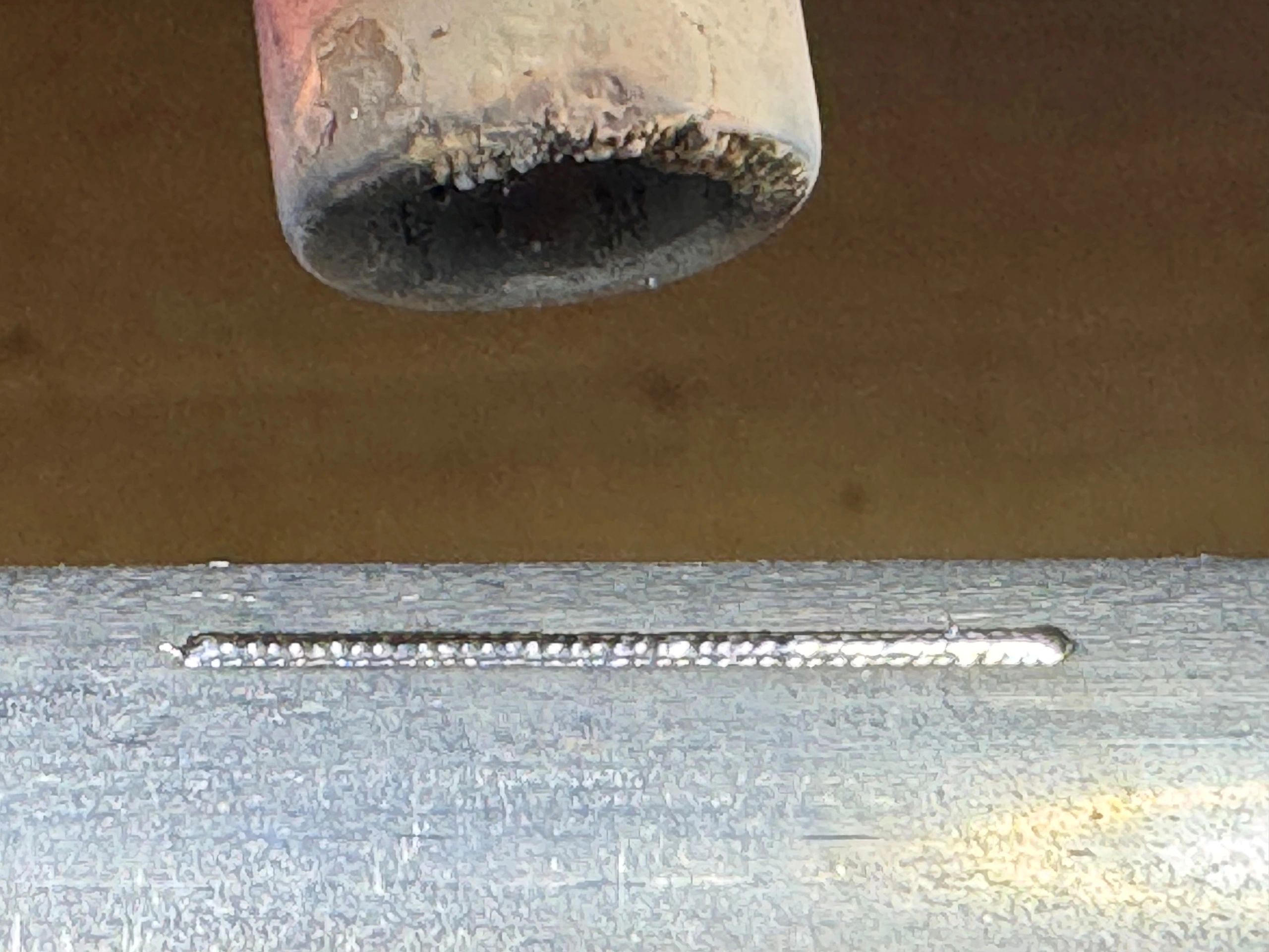 Close-up of a worn welding torch tip and a welded metal seam.