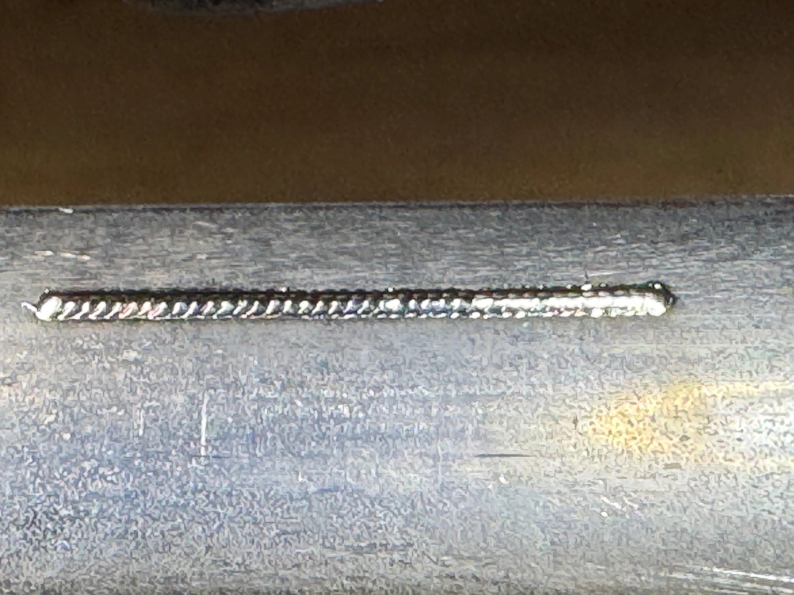 Close-up of a metallic welded seam on a gray surface.