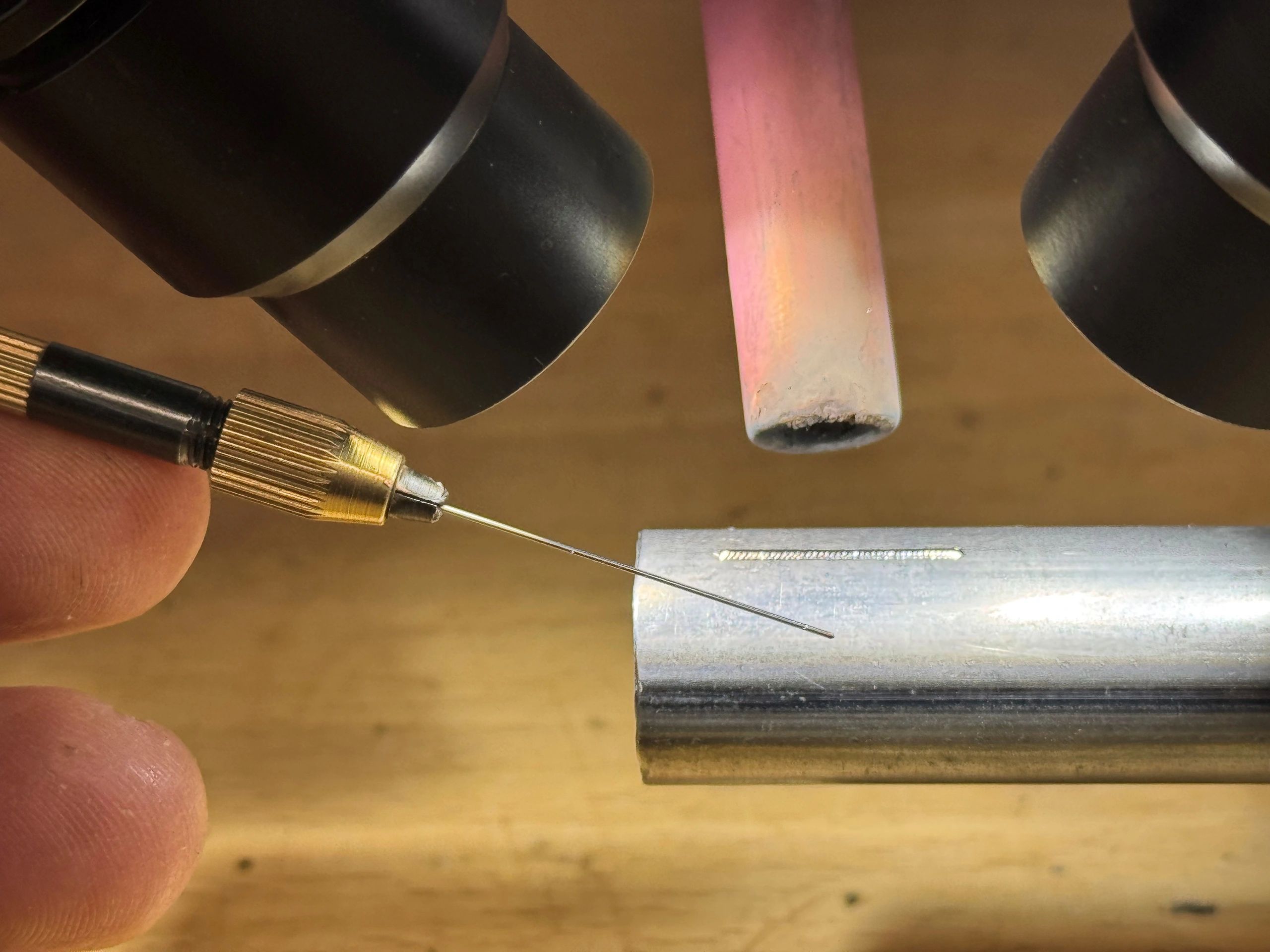 Close-up of soldering iron tip near a metal piece under a microscope.