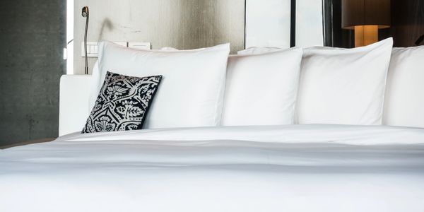 A neatly made bed with white pillows and a decorative black and white cushion.