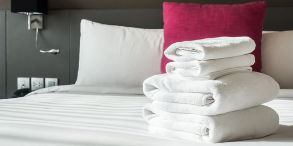 Stack of white towels on a neatly made bed with white and pink pillows.