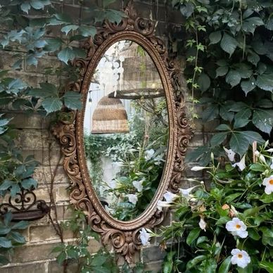 Ornate oval mirror on a brick wall surrounded by green ivy and white flowers.
