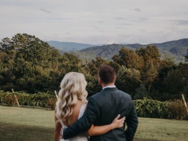 Couple in formal attire embraces while overlooking a scenic mountain landscape.