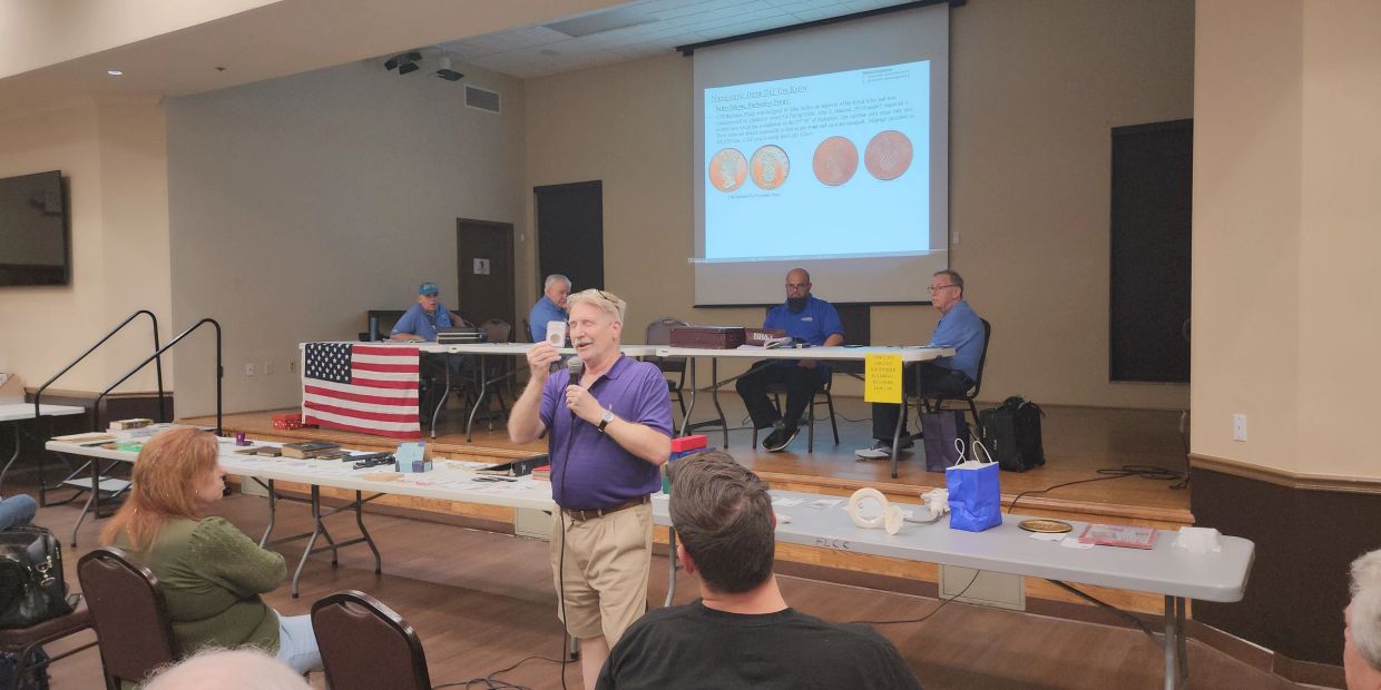 A man giving a presentation about coins to an audience in a community hall.