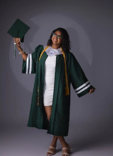 Graduate in gown holding cap and smiling.