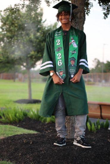 Graduate in green cap and gown posing outdoors.