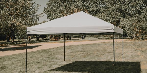 A white canopy tent set up on a grassy area in a park.