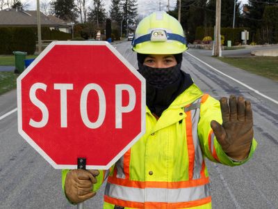 Construction worker holding a stop sign and signaling to stop on a road.