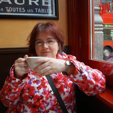 A woman in a colorful coat enjoys a hot beverage at a cozy café.