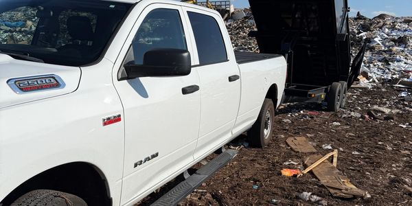 White Ram 2500 truck with a black dump trailer at a landfill site.