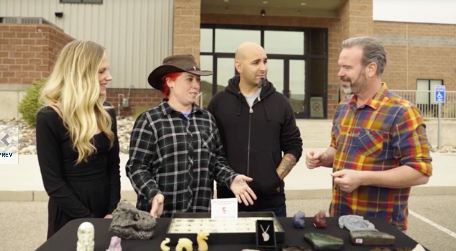 Four people talking around a table with various small sculptures outdoors.