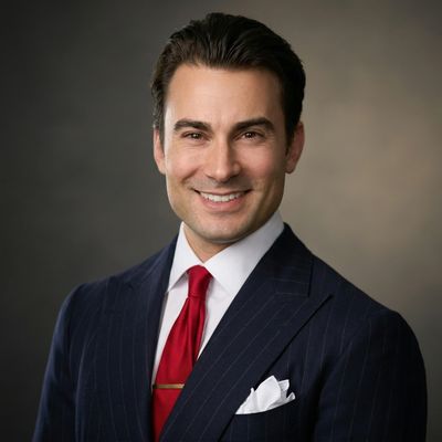 Confident man in a dark pinstripe suit and red tie smiling against a neutral background.