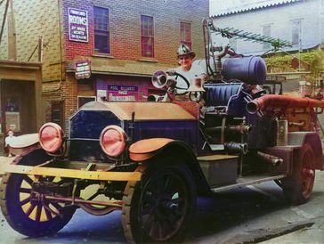 Vintage fire truck with a firefighter in uniform posing on it.
