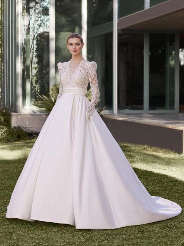 Elegant bride in a long-sleeve lace and satin wedding gown outdoors.