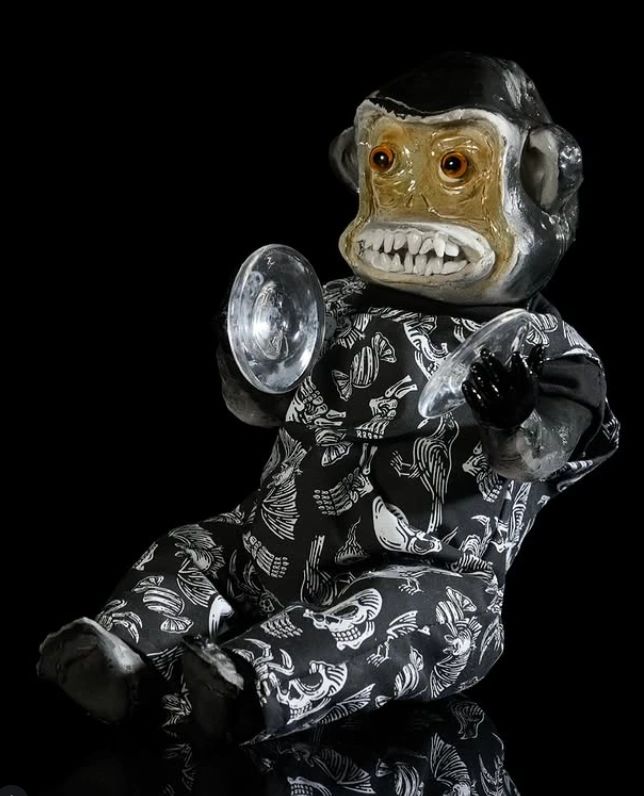 Creepy monkey toy with a grimace, dressed in skeleton-patterned clothes, holding cymbals.