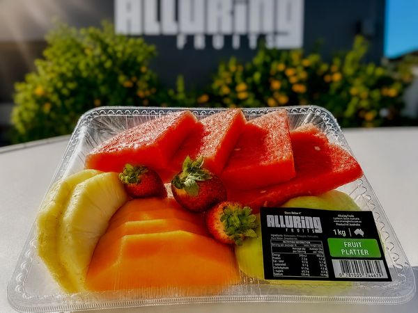 Fresh fruit platter with watermelon, strawberries, pineapple, and melon in a clear container.