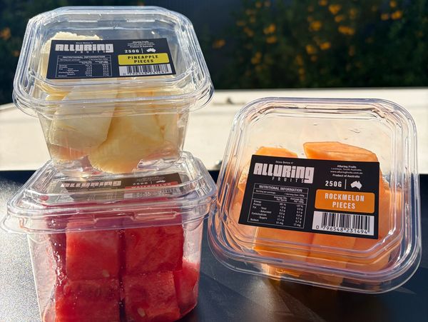 Three containers of fresh fruit pieces labeled Alluring Fruits on a table outdoors.