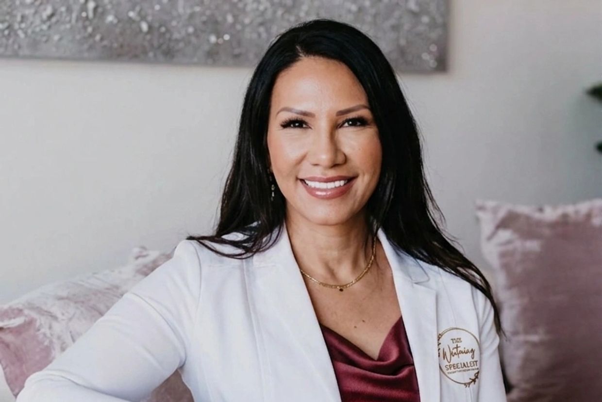 A smiling woman in a white coat and maroon top.