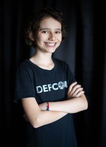 Smiling young person wearing a DEFCON t-shirt with arms crossed.