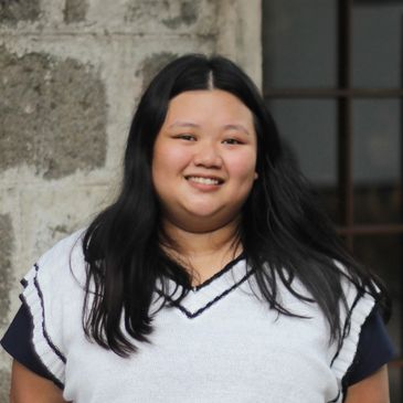 Smiling woman with long black hair wearing a white sweater vest.