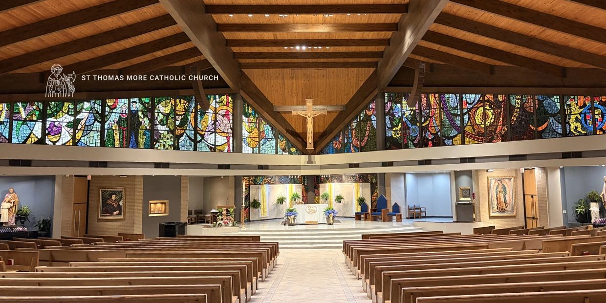 Interior of St Thomas More Catholic Church with wooden pews and stained glass windows.