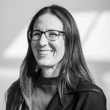 Black and white portrait of a smiling woman with glasses and long hair.