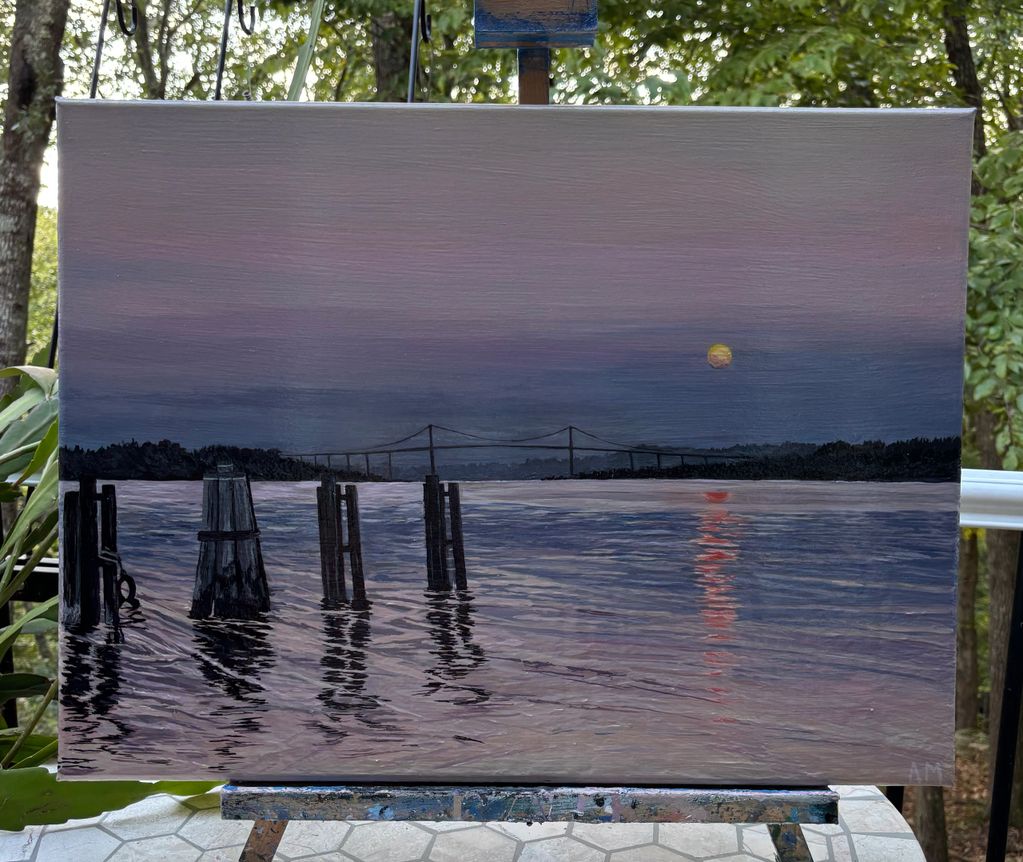 Sunset over a calm river with a bridge and wooden posts.