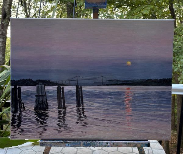 Sunset over a calm river with a bridge and wooden posts.
